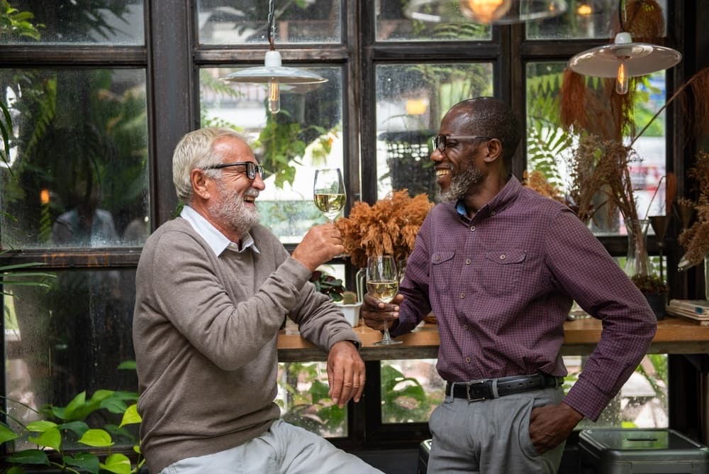 Two friends laughing over glasses of wine in a garden café