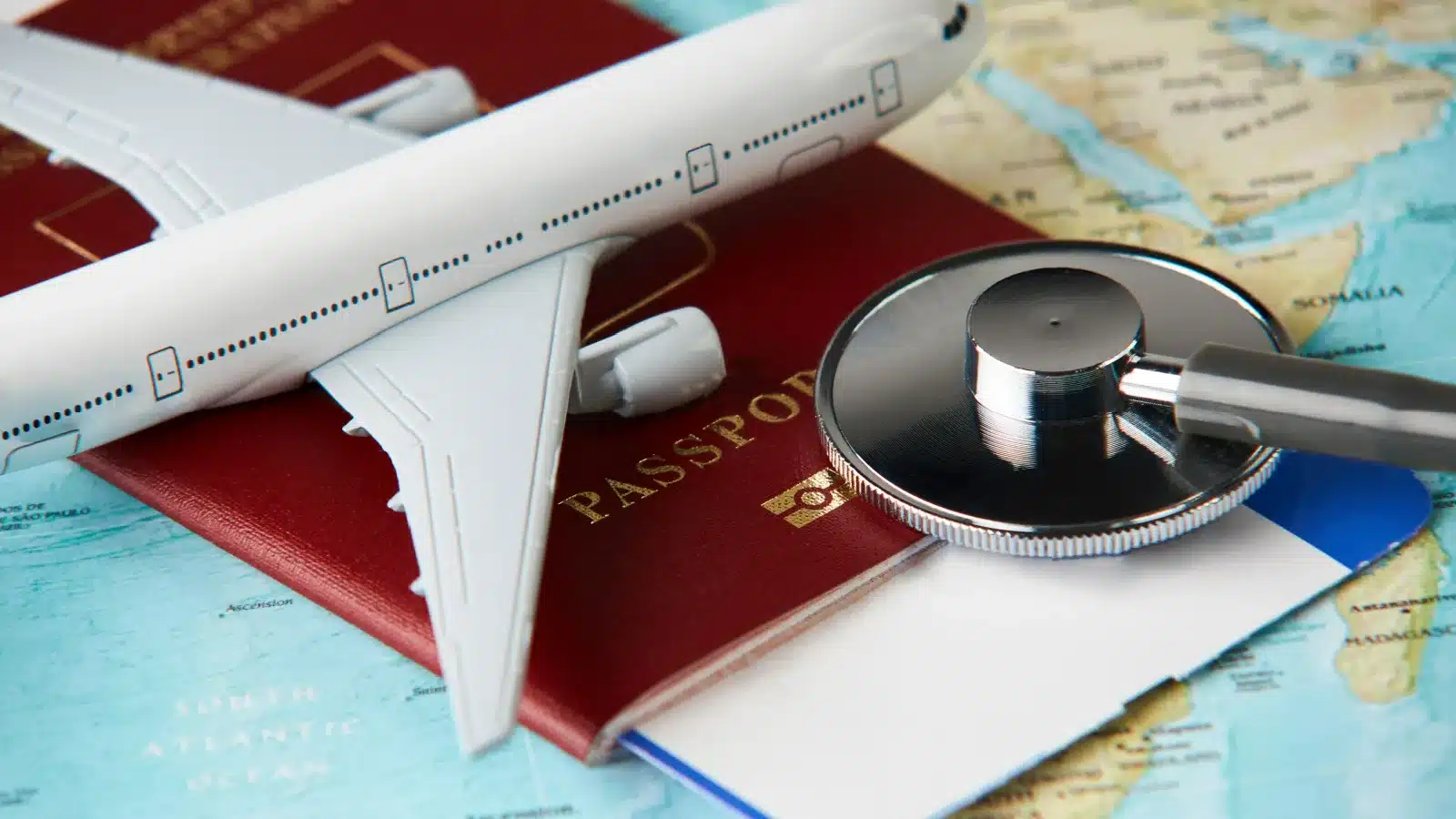 A passport, a model plane and a stethoscope on a world map